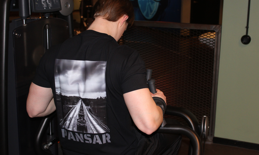 Person i svart PANSAR-t-shirt tränar rygg i en gymmaskin. Bilden på tröjans rygg visar en svartvit militärkolonn med stridsfordon på en landsväg.